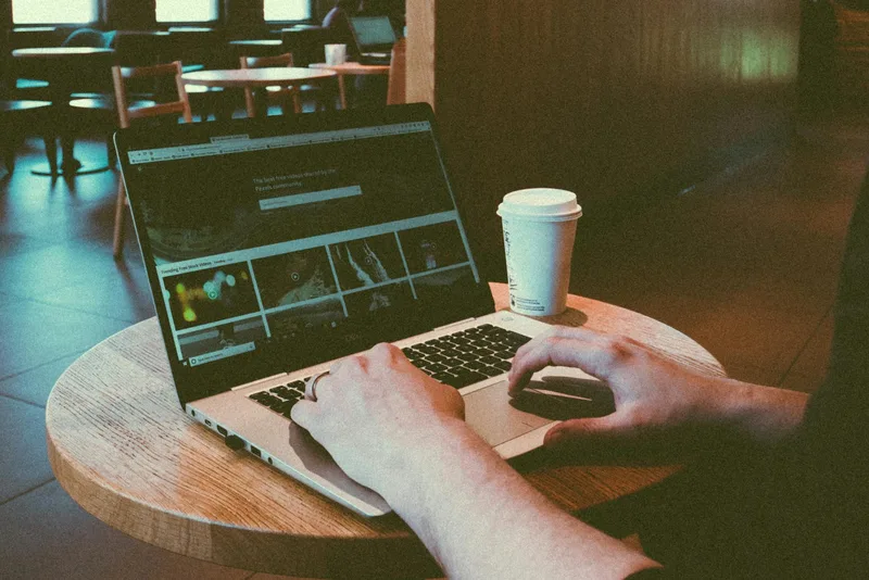 Person typing on a laptop in a cozy café — the kind of remote work setup creators use to manage their lead magnet funnels
