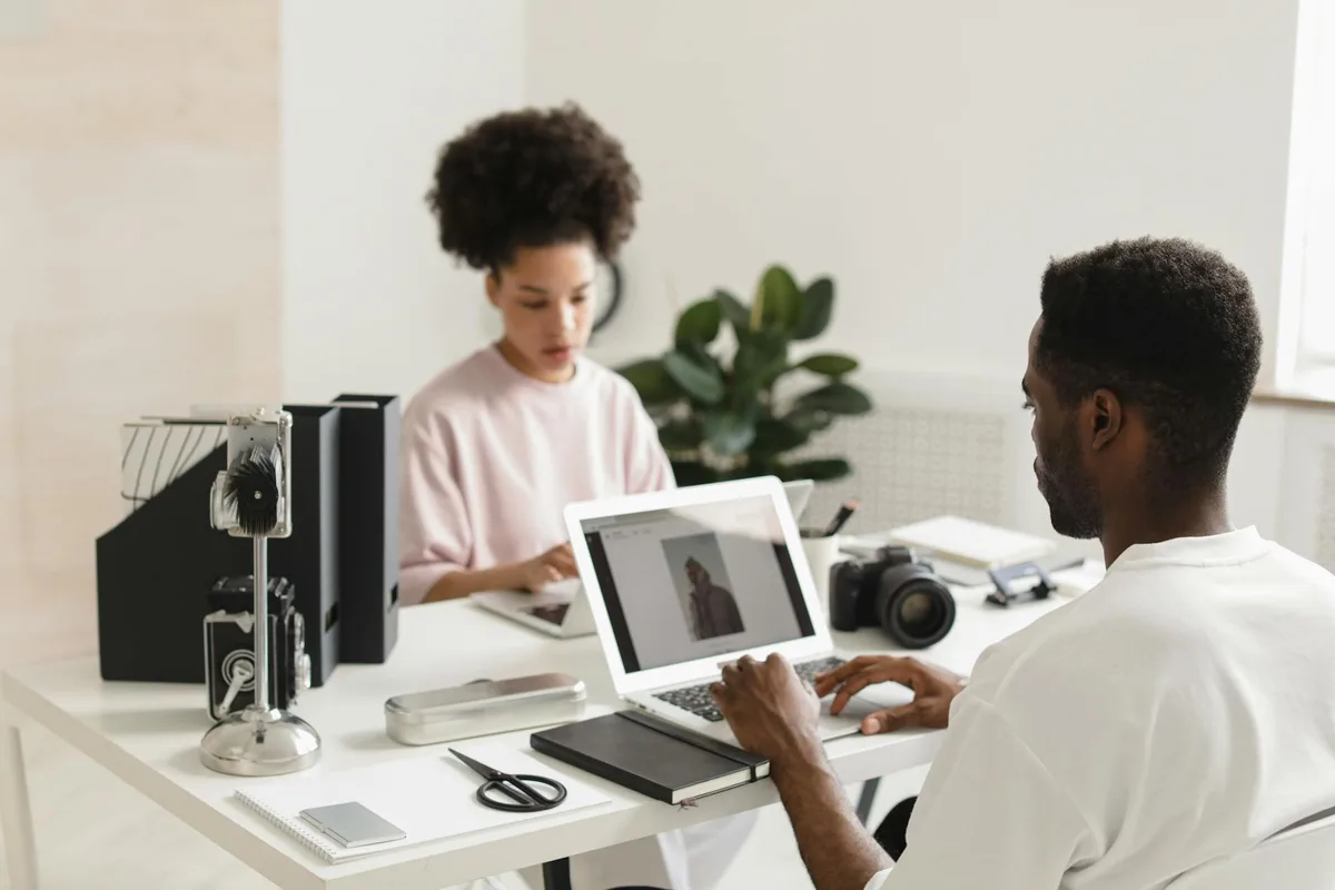 Two creators collaborating over laptops in a bright modern office space — planning a digital project together