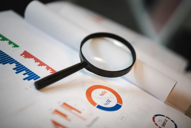 Magnifying glass over documents representing a thorough review of the lead magnet delivery flow to catch invisible leakage points